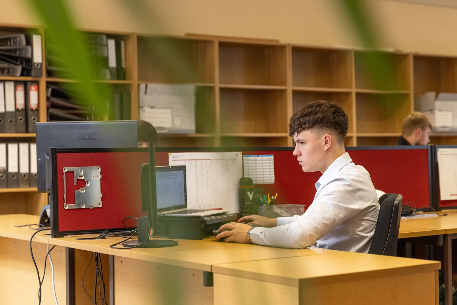 Young office worker sitting at a desk focused on a computer screen in a professional workspace.