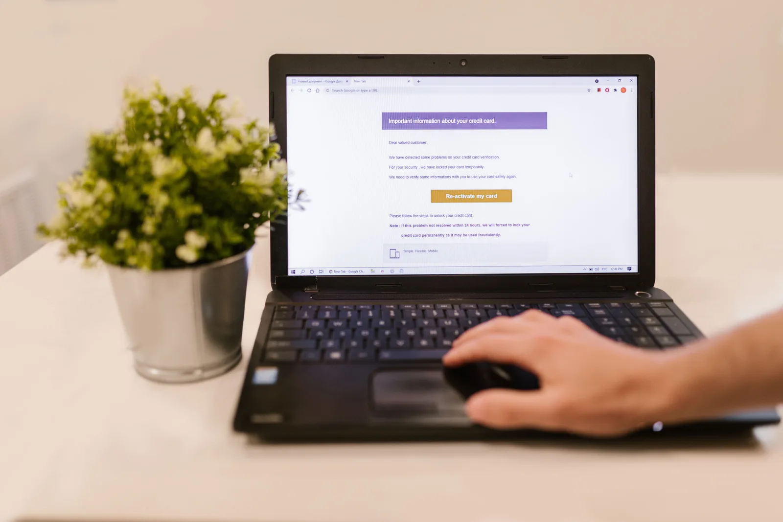 Hand using a laptop trackpad next to a small green plant on a white desk.