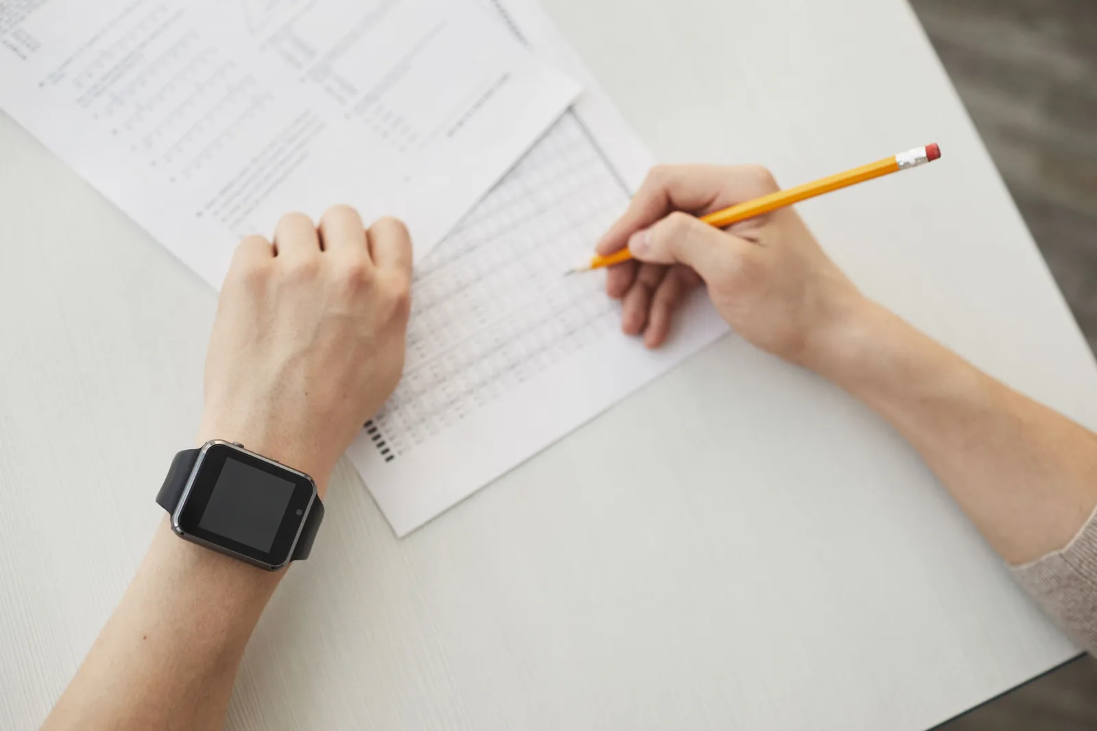 Person filling out a paper time log while wearing a smartwatch.
