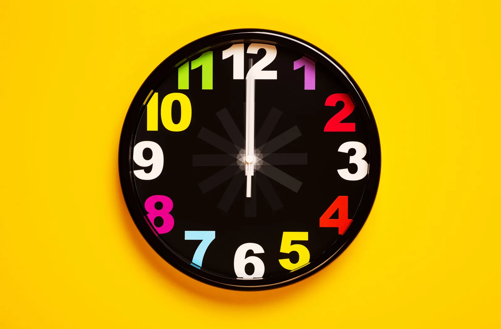 Black analog clock with colorful numbers on a yellow background symbolizing the 40-hour week in Spain.