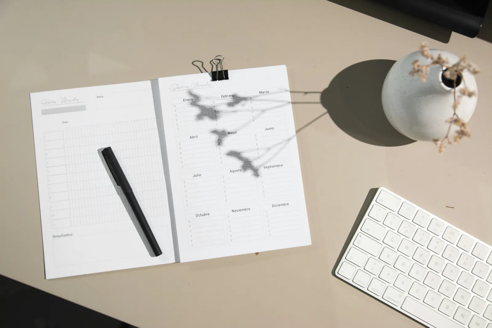 Paper habit tracker and black pen on a desk next to a white computer keyboard.