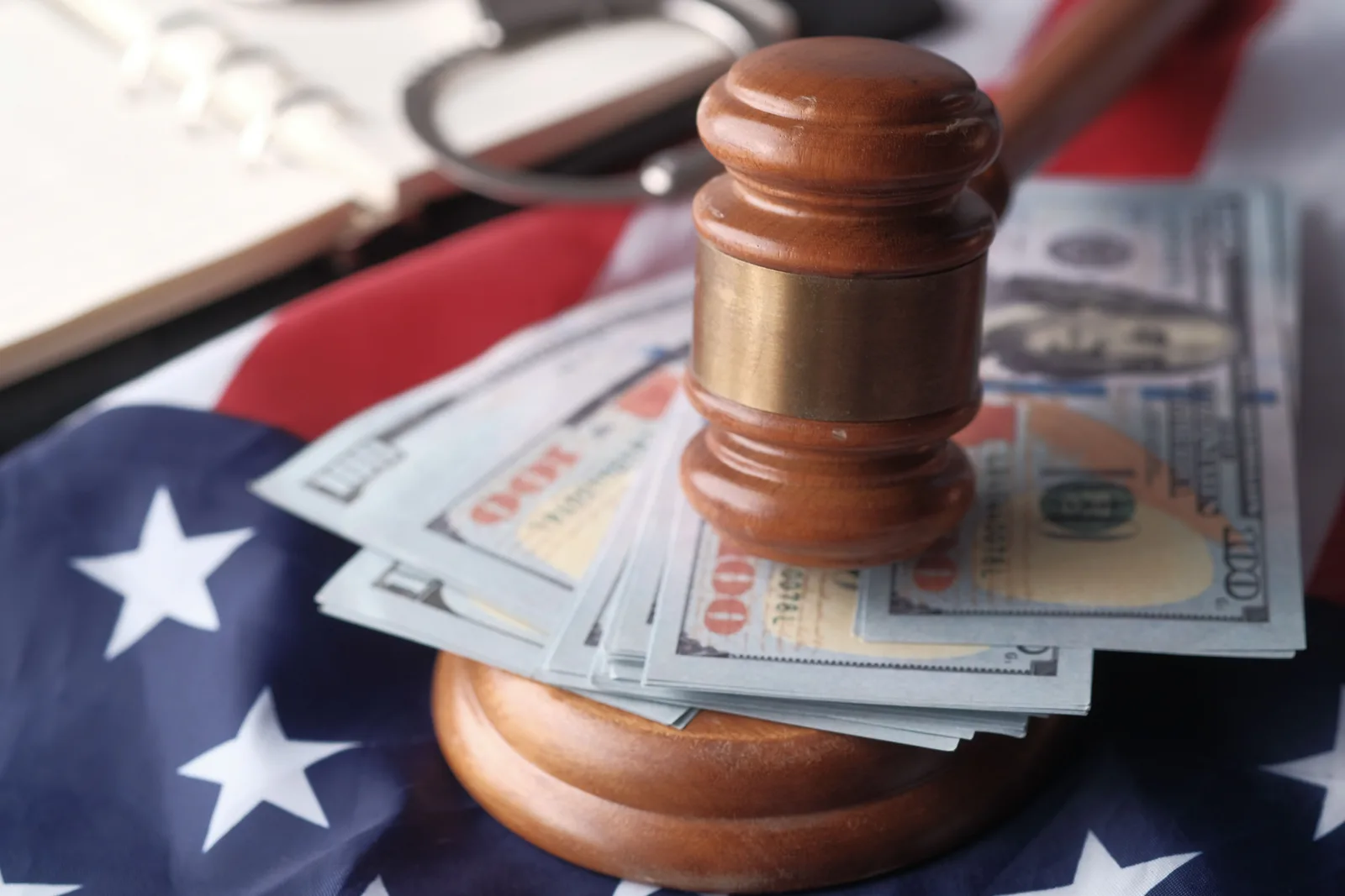 Wooden gavel resting on a stack of hundred dollar bills over a US flag.